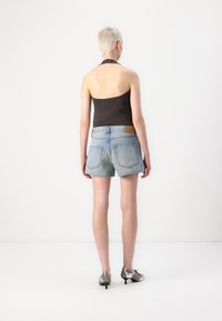Shorts en denim bleu clair avec une coupe regular et un ourlet effiloché, associés à un haut halter noir et des escarpins argentés à bout pointu.