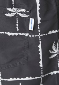 Melna auduma ar baltu palmu koku rakstu un režģa līnijām. Iekļauj kabatu un zilu "JACK & JONES" etiķeti sānos.
