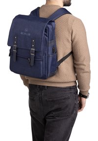 Sac à dos en tissu bleu marine avec double rabat supérieur, poche frontale zippée, bretelles ajustables et accents en cuir noir. Possède un extérieur texturé.