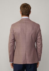 Blazer à carreaux marron en tissu texturé avec une coupe ajustée. Dispose de revers crantés, d'évents latéraux et d'une fermeture à deux boutons.