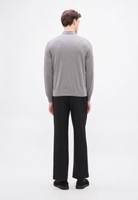 Pulover gri tricotat cu guler, vedere din spate care arată mânecile lungi și tivul cu model reiat. Asortat cu pantaloni largi negri și pantofi negri.