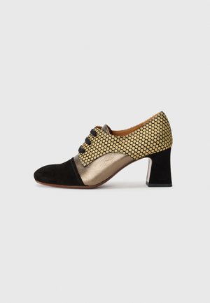 Women's low-heeled shoe with black toe, metallic gold midsection, and gold polka dot pattern on upper with black laces.
