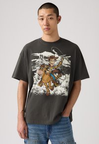 Camiseta de gran tamaño en color gris con un gráfico de un vaquero de dibujos animados montando un caballo, con colores vibrantes y una impresión ligeramente texturizada.