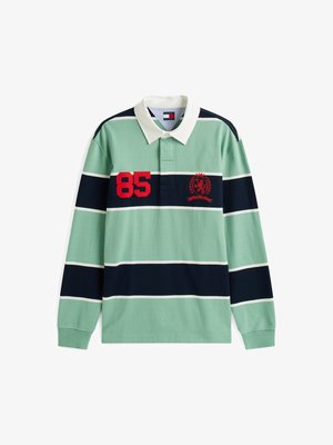 Pitkähihainen poolopaita, jossa on vihreä ja laivastonsininen raidoitus. Mukana valkoinen kaulus, punainen numero "85" ja brodeerattu vaakuna rinnassa.