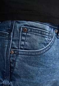 Lyseblå denimjeans med forreste lomme, kobbernitter og kontrasterende syningsdetaljer. Glat tekstur og klassisk snit.