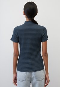 Tmavě modrý top s krátkým rukávem a texturovaným, žebrovaným vzorem. Má vysoký límec a je kombinován s světlými džínami.