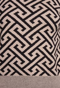 Pull en tricot présentant un motif géométrique en noir et beige. Tissu texturé avec un ourlet côtelé et un design distinct en forme de labyrinthe.