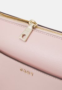 Zbliżenie na różową skórzaną torbę z złotym zamek błyskawicznym i logo DKNY. Materiał ma teksturowaną powierzchnię; projekt jest elegancki i prostokątny.