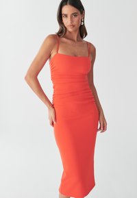 Elegantes oranges Midikleid mit dünnen Spaghettiträgern, das an den Seiten eine geraffte Textur und eine figurbetonte Silhouette aufweist.