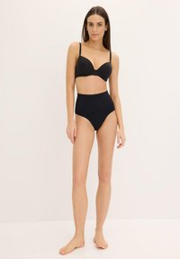 Soutien-gorge noir rembourré avec armatures et bretelles réglables, associé à des culottes taille haute noires en tissu lisse.