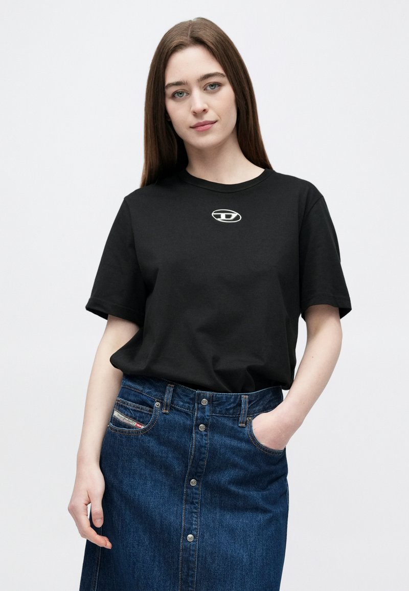 Black cotton t-shirt with a round neckline and short sleeves, featuring a small silver logo on the chest, paired with a blue denim skirt.