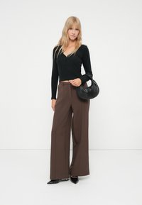 Čierny cropped top s dlhými rukávmi, hnedé široké nohavice a čierna kabelka. Oblečenie má zapínanie na gombíky a hladkú textúru.