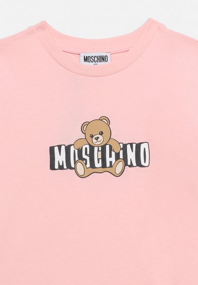 Ροζ παιδικό μπλουζάκι με ένα καφέ αρκουδάκι να κάθεται πάνω από το ασπρόμαυρο κείμενο "MOSCHINO" στο μπροστινό μέρος.