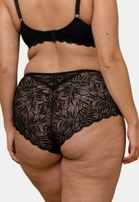 Culotte en dentelle noire avec motifs floraux, bords festonnés et design couvrant entièrement. Le matériau est transparent et texturé.