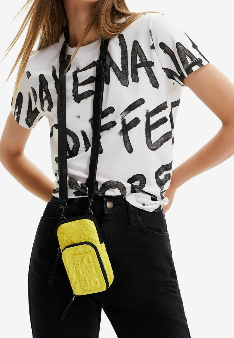 Black and white graphic T-shirt with bold text, paired with a bright yellow textured crossbody bag featuring a logo and zippers.
