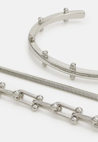 Three pieces of silver-toned jewelry: a round cuff with spherical accents, a flexible chain with ribbed texture, and a linked chain with spheres.