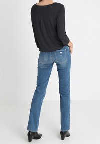 Svart topp med prickar och rund halsringning samt långa ärmar, tillsammans med blå raka jeans med diskret blekning och bakfickor.