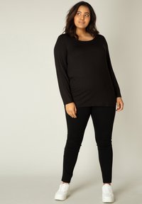 Zwarte lange mouw top gecombineerd met zwarte leggings en witte sneakers. De stof lijkt glad en aansluitend, met een ronde halslijn.