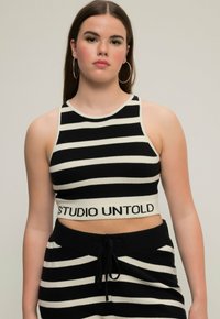 Černobílý pruhovaný pletený crop top s kulatým výstřihem a logem "STUDIO UNTOLD" na spodním lemu, s přiléhavým střihem a ribbovanou texturou.