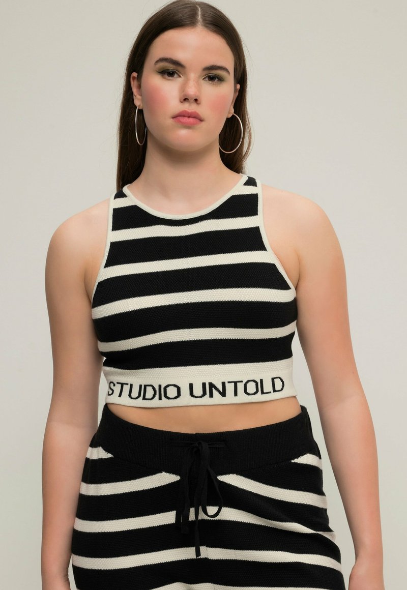 Černobílý pruhovaný pletený crop top s kulatým výstřihem a logem "STUDIO UNTOLD" na spodním lemu, s přiléhavým střihem a ribbovanou texturou.