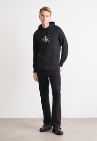 Felpa nera con cappuccio e tasca frontale, caratterizzata da un design del logo contrastante. Abbinata a jeans neri a gamba dritta e scarpe nere.