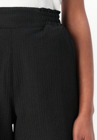I pantaloni neri con texture presentano una vita elastica arricciata e tasche laterali. Il tessuto ha un motivo a coste per un dettaglio aggiuntivo.