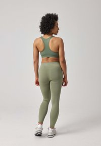 Set di abbigliamento attivo verde oliva composto da un reggiseno sportivo aderente con design a schiena scoperta e leggings a vita alta con una texture liscia.