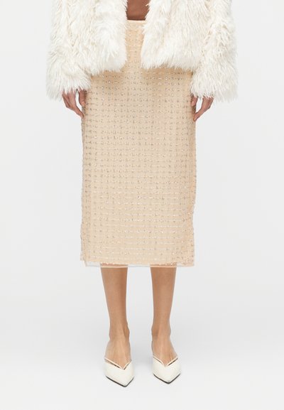 Jupe midi beige en tissu texturé à motif quadrillé, ornée d'accents scintillants. Associée à des chaussures blanches à bouts pointus.