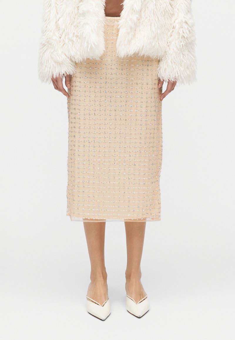 Jupe midi beige en tissu texturé à motif quadrillé, ornée d'accents scintillants. Associée à des chaussures blanches à bouts pointus.