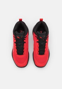 Chaussures de sport rouges avec accents noirs, tige en maille, fermeture à lacets, col rembourré et semelles noires contrastantes. Logo de la marque notable visible.