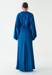 Lange, vloeiende jurk van levendig blauw satijn met losse mouwen, een getailleerde taille en een ritssluiting aan de achterkant. Gladde textuur en elegante silhouet.