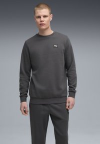 Dunkelgrauer Sweatshirt aus weichem Stoff mit rundem Halsausschnitt, gerippten Bündchen und kleinem Puma-Logo auf der Brust. Kombiniert mit passenden Hosen.