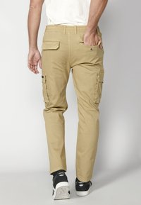 Khaki cargo nohavice s elastickým pásom, dvoma bočnými vreckami a dvoma zadnými vreckami. Hladká tkanina s normálnym strihom a zúženými nohavicami.