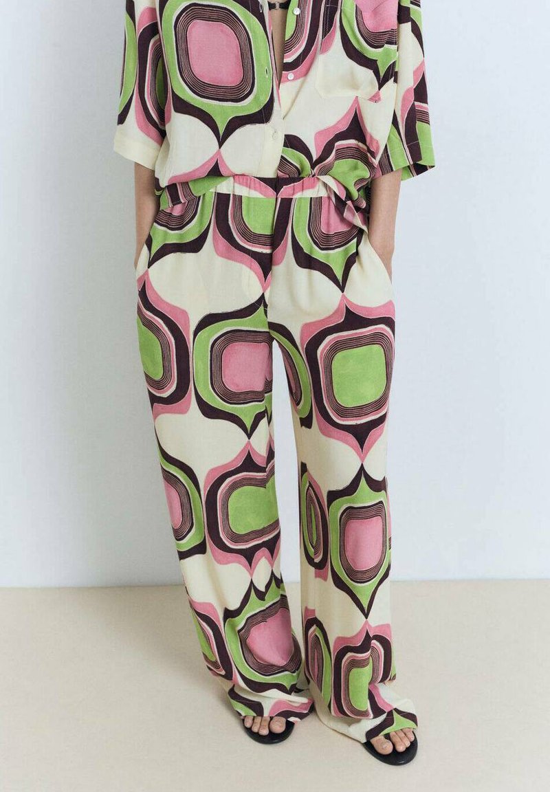 Muster-Jumpsuit mit pastellrosa, grünen und schwarzen Formen auf cremefarbenem Hintergrund; lockere Passform mit kurzen Ärmeln und seitlichen Taschen.