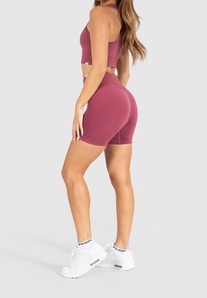 Top corto sportivo bordeaux e pantaloni shorts, tessuto a costine, design aderente, abbinato a sneakers bianche con accenti neri, visto da dietro.