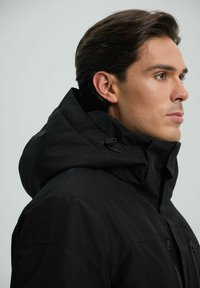 Giacca nera con cappuccio, colletto alto, chiusura con zip e coulisse regolabile. Tessuto liscio con un design minimalista e senza motivi visibili.