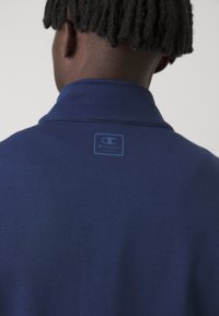 Mørkeblå polo skjorte med tekstureret stof og et lille logo label på den bageste krave. Har et klassisk kravedesign.