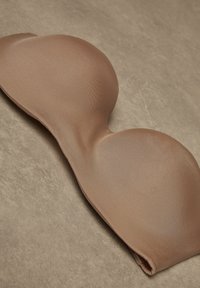 Nahtloser, gepolsterter trägerloser BH in hellbrauner Farbe, aus glattem Material mit weicher Textur, mit konturierten Cups und einem eleganten Design.