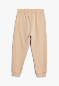 Pantalones de chándal beige hechos de una tela suave, con una cinturilla elástica acanalada y puños, con una textura lisa y un corte relajado.