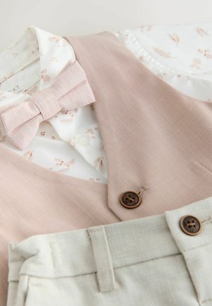 Jasnoróżowa kamizelka z teksturowanej tkaniny, biała koszula w kwiatowy wzór, różowa mucha oraz jasnoszare spodnie z brązowymi guzikami.