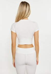 Fehér, rövidujjú, cropped sportfelső, kerek nyakkivágással, magas derekú fehér leggingsszel párosítva, sima textúrával, minimális részletezéssel.
