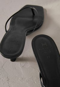 Sandali neri flat con cinturini sottili, design a punta quadrata e texture in pelle liscia. Presentano un marchio impressa sulla suola.