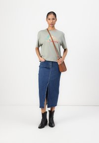 Light green short-sleeve T-shirt with "Cowgirls" graphic, paired with a fitted denim skirt featuring a front slit. Black ankle boots and brown bag.