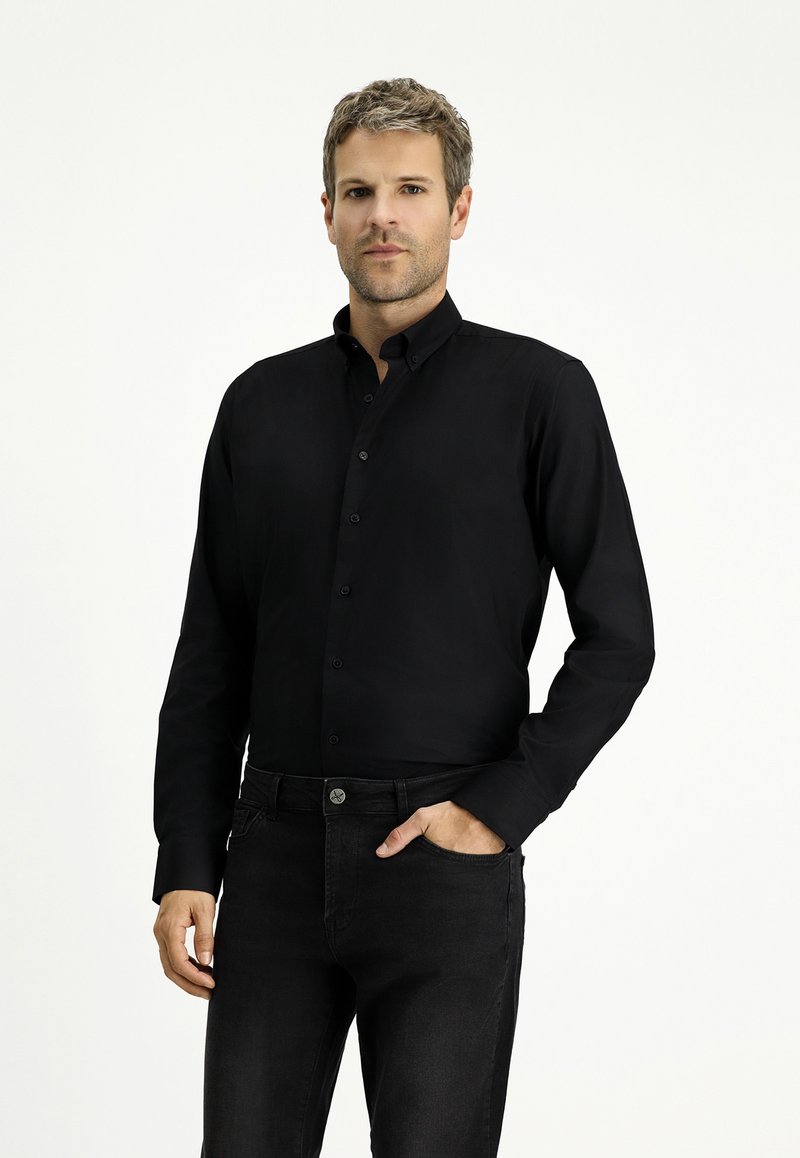 Camicia nera a maniche lunghe con bottoni e colletto classico. Tessuto liscio, design aderente e leggero lucido. Abbinata a jeans in denim scuro.