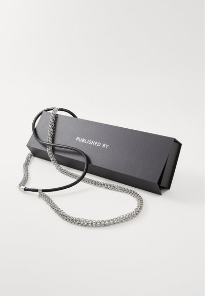 Silver chain necklace with a leather accent, laid next to a black rectangular box that has "PUBLISHED BY" printed on it.