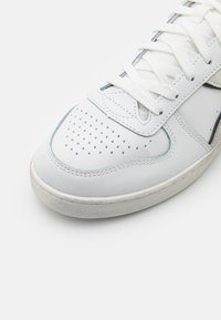 Sneaker bianco con parte superiore in pelle, punta perforata, lacci piatti, accentuazione grigia lungo la suola e suola in gomma texture.