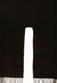 Écharpe noire avec une découpe centrale, présentant des bords à franges et des détails de motif subtils le long des côtés verticaux. Texture lisse.