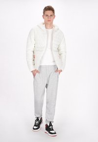 Witte pufferjack met een capuchon, met een gestructureerde afwerking, gecombineerd met lichtgrijze sweatpants en zwarte high-top sneakers met rode accenten.