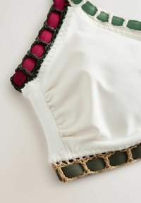 Gros plan d’un tissu blanc avec un détail froncé et une bordure tissée en vert, beige, noir et rouge sur une surface plane.
