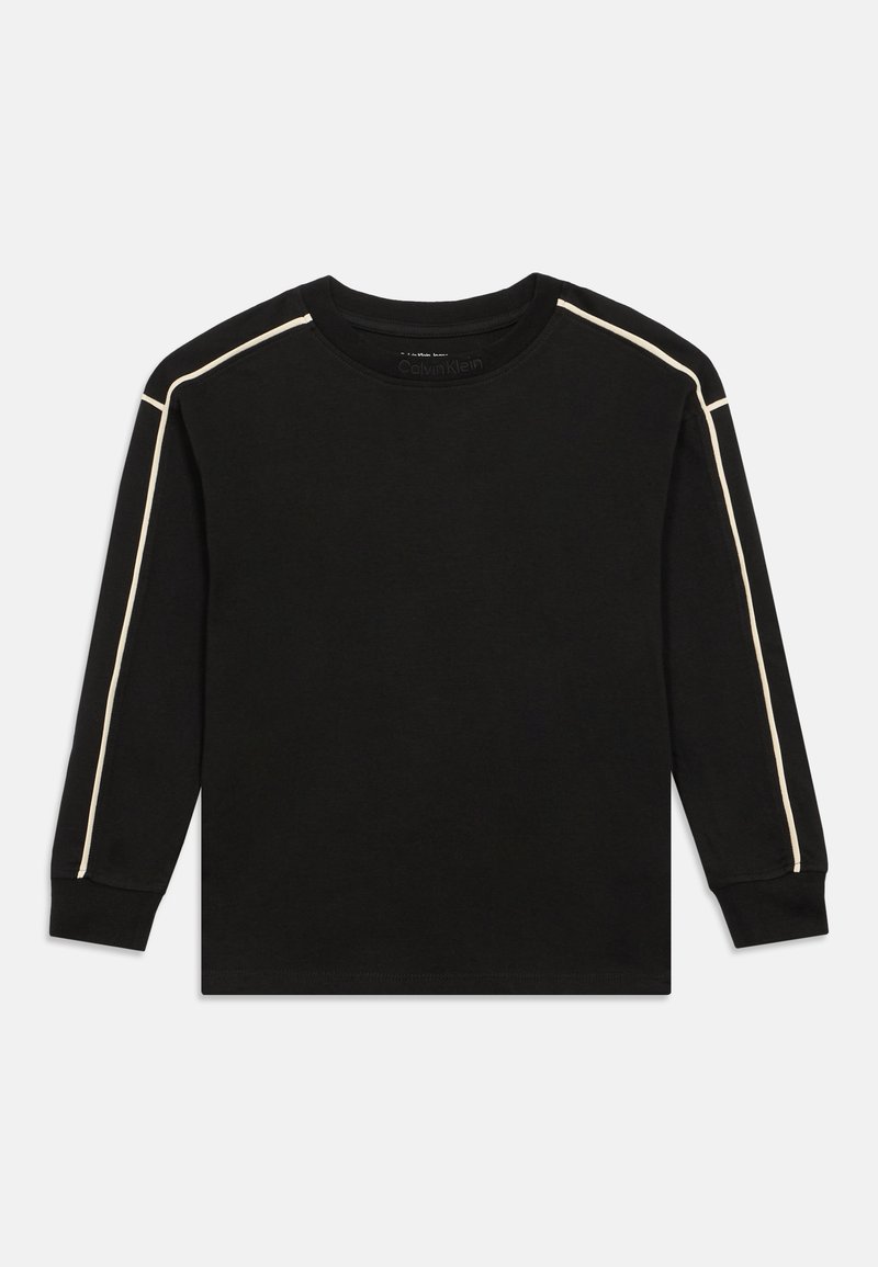 Melna gara piedurkne T-kreklā ar apaļu kakla izgriezumu, kas apvilkta ar kontrastējošām gaismas bežām sānu svītrām gar pleciem un piedurknēm.